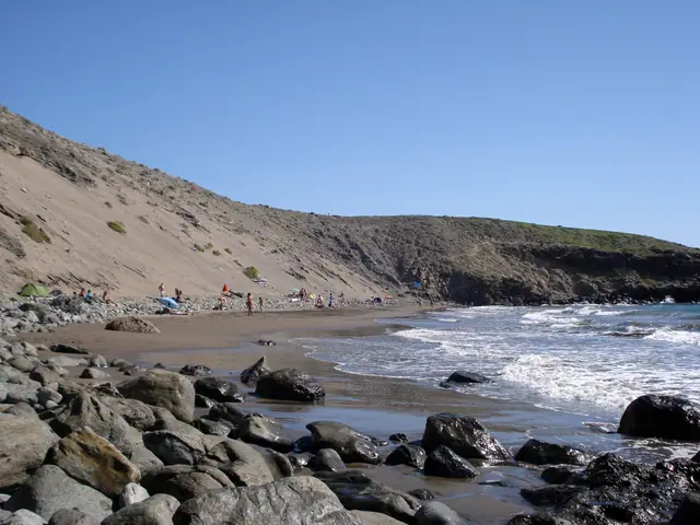 Playa de Las Carpinteras beach in Gran Canaria, featuring a pebbly shoreline with calm water conditions