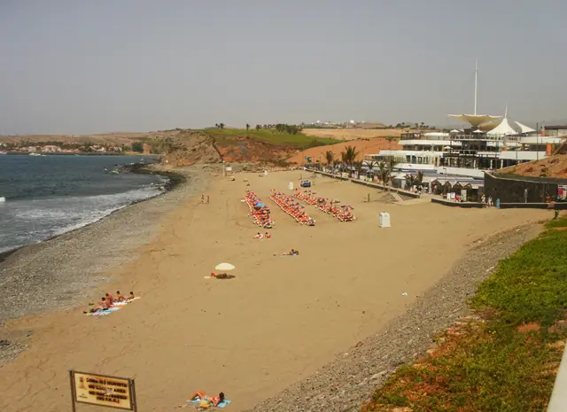 Playa Meloneras beach in Gran Canaria, featuring a sandy shoreline with calm water conditions, certified with Blue Flag status for environmental quality