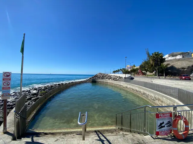 Playa de Arguineguín beach in Gran Canaria, featuring a pebbly shoreline with calm water conditions